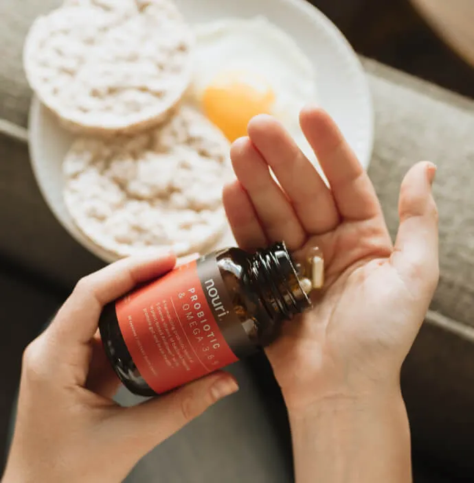 Hand met een supplementcapsule naast een ontbijt met rijstwafels en ei